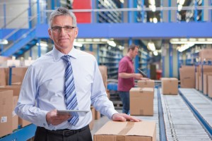 Portrait of smiling businessman holding digital tablet at conveyor belt in distribution warehouse Image downloaded by anonymous anonymous at 12:25 on the 10/04/16